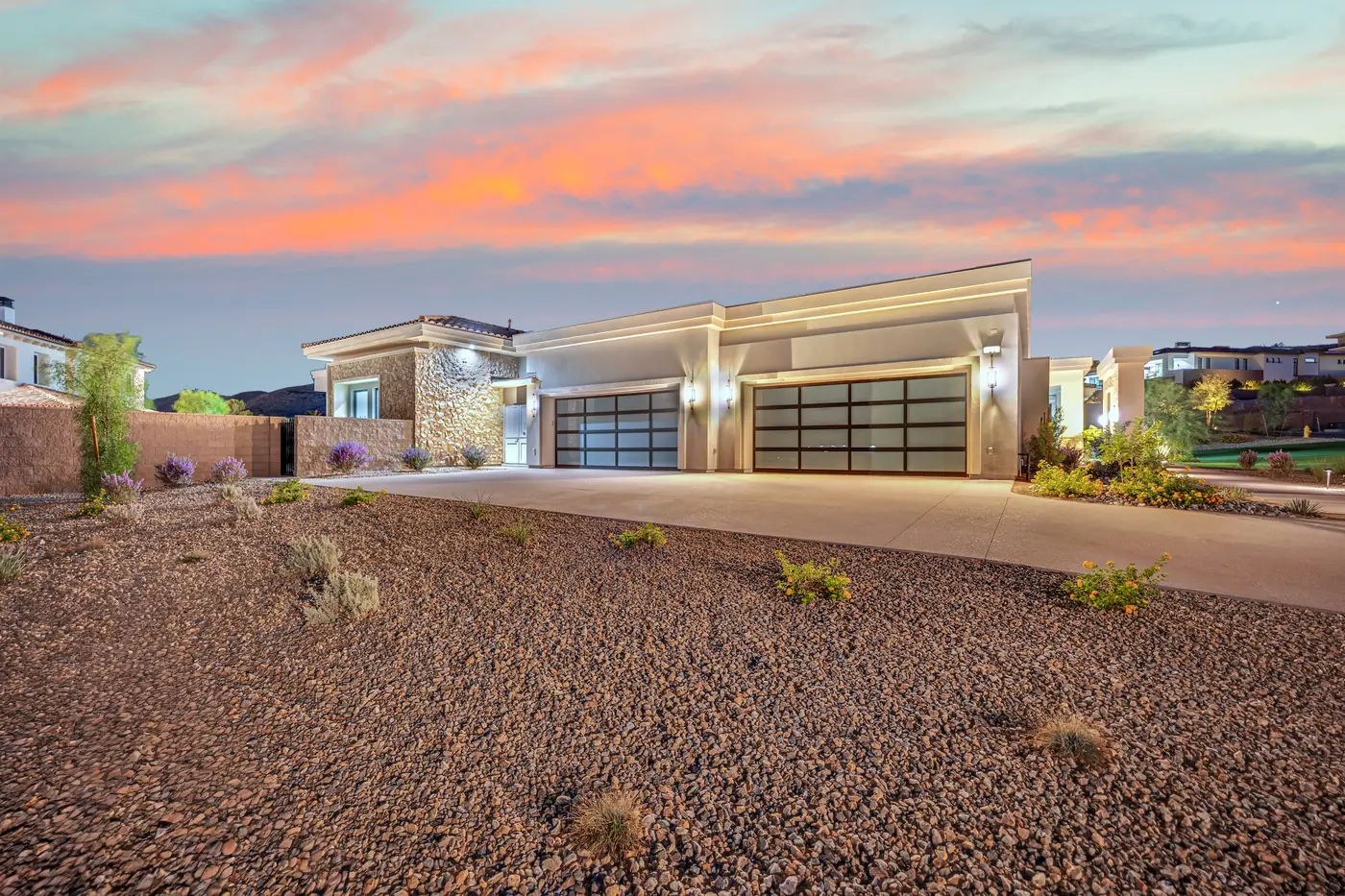 Front elevation at dusk with the garage lit and desert planting in front