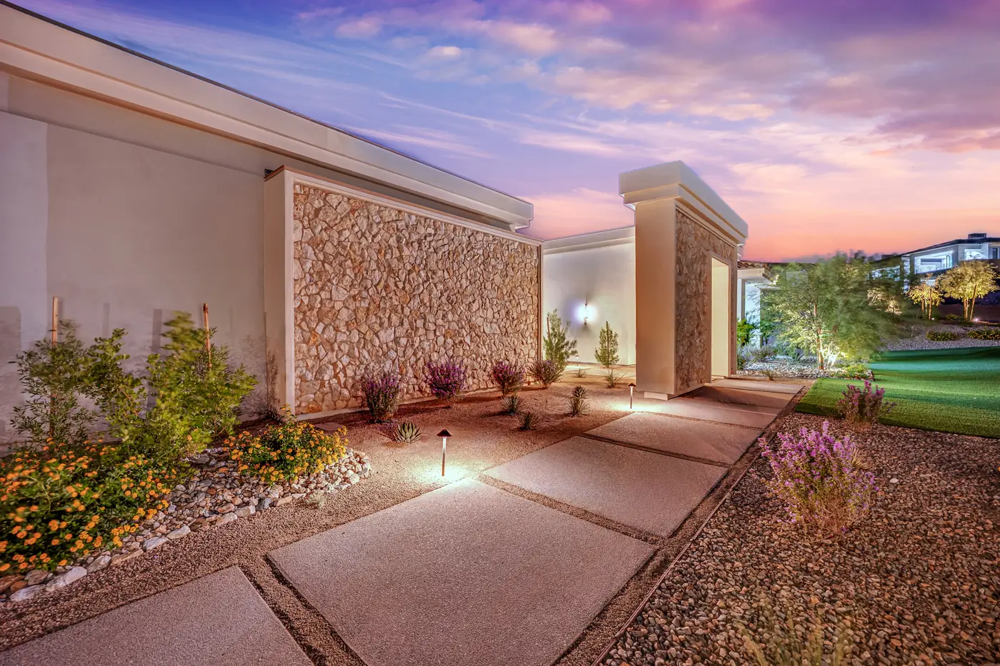 The entry walk at dusk with the stone wall lit from below