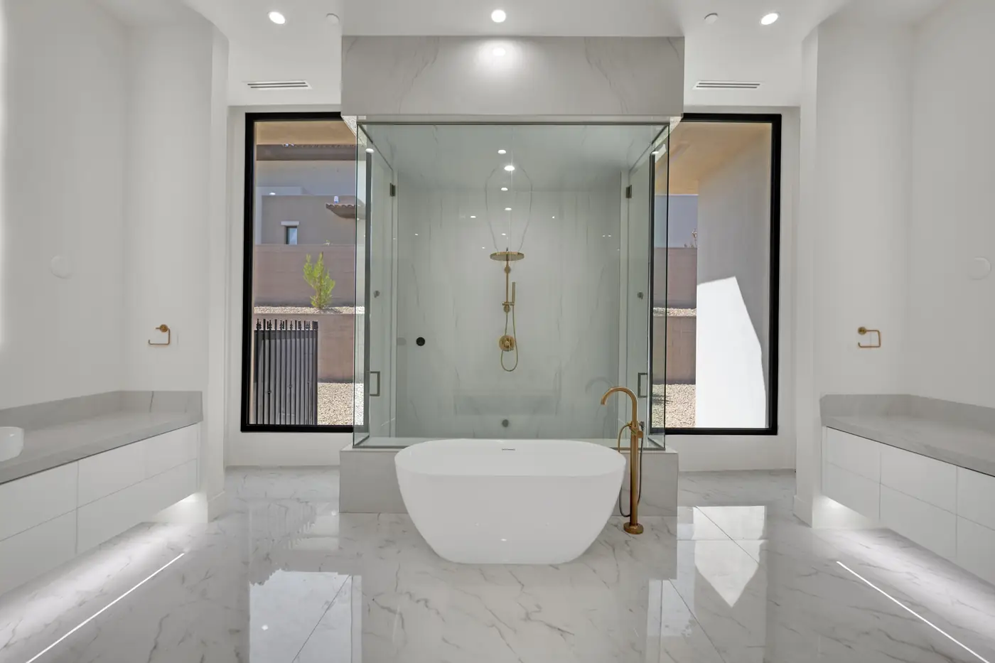 Primary bath with a freestanding tub between twin vanities and a glass shower behind